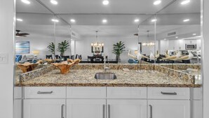 A modern kitchen with granite countertops, white cabinets, and a large mirror above the sink.