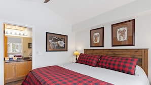 A bedroom with a large bed, wooden headboard, and a mirror with lights. There are two framed pictures on the wall. - Quail Run Townhomes - Long Term Only - 30+ nights - Spacious, Garage, W/D, BBQ (Steamboat Springs)