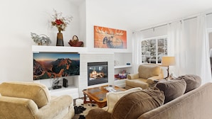 A cozy living room with a fireplace, comfortable seating, and a scenic painting above it. - Quail Run Townhomes - Long Term Only - 30+ nights - Spacious, Garage, W/D, BBQ (Steamboat Springs)