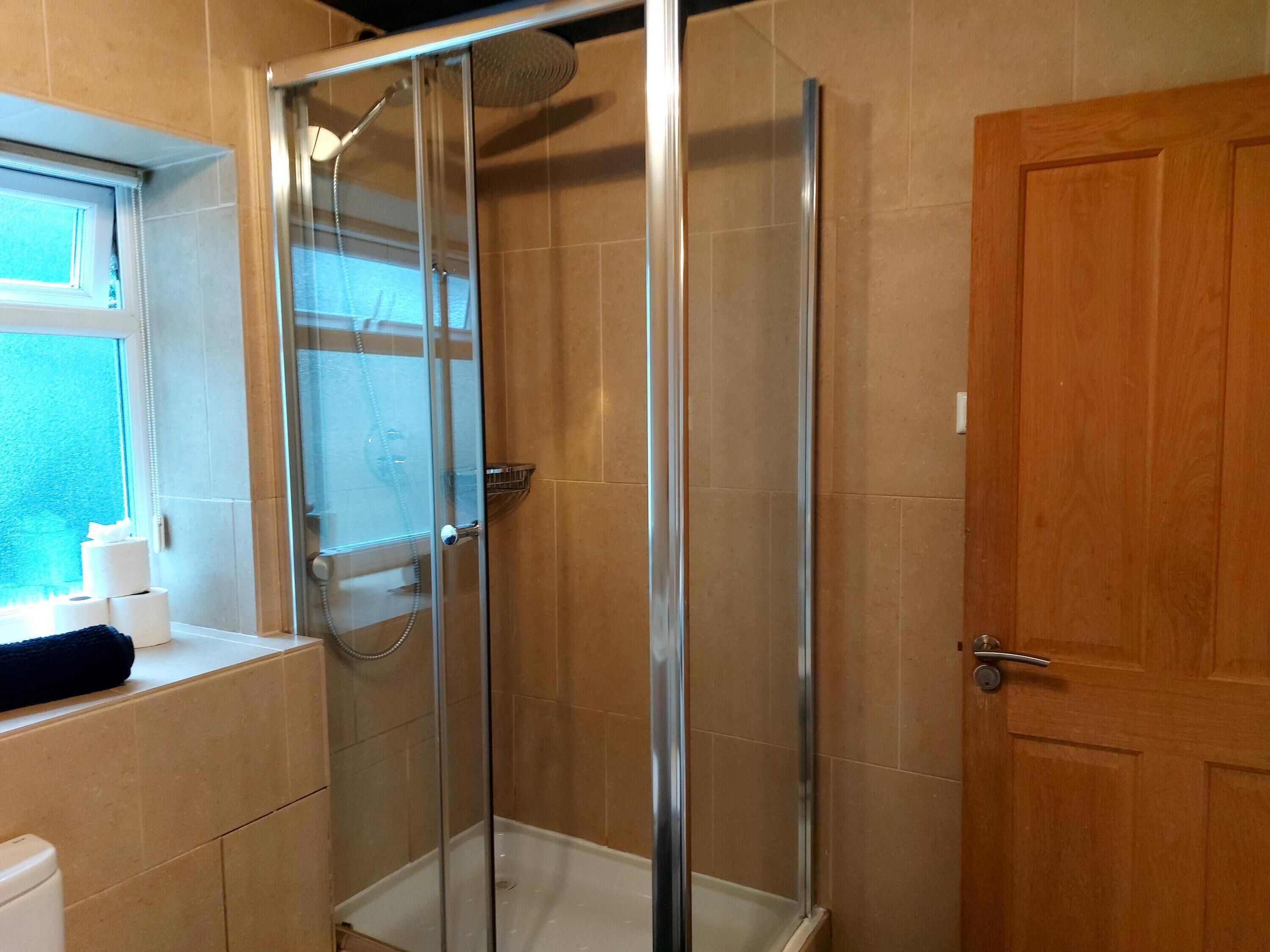 Eine Dusche mit Glastür, eine Holztür und ein Fenster mit Handtuch und Toilettenpapier.