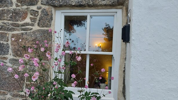 A stone wall with a white window and pink flowers in front. - Kitts Cottage in Redruth (Redruth)