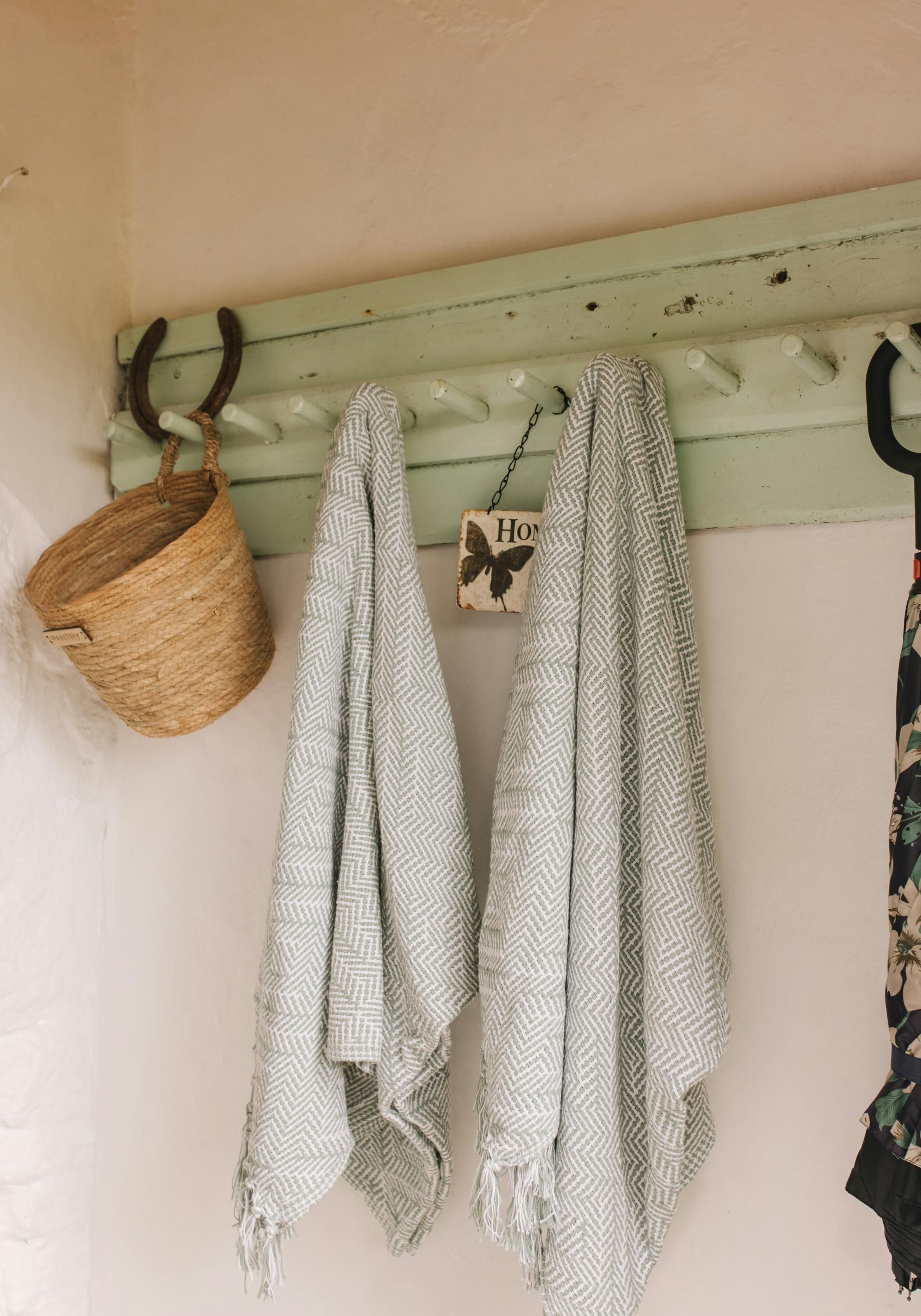 A wall-mounted coat rack with two patterned scarves, a woven basket, and a small sign with a butterfly.