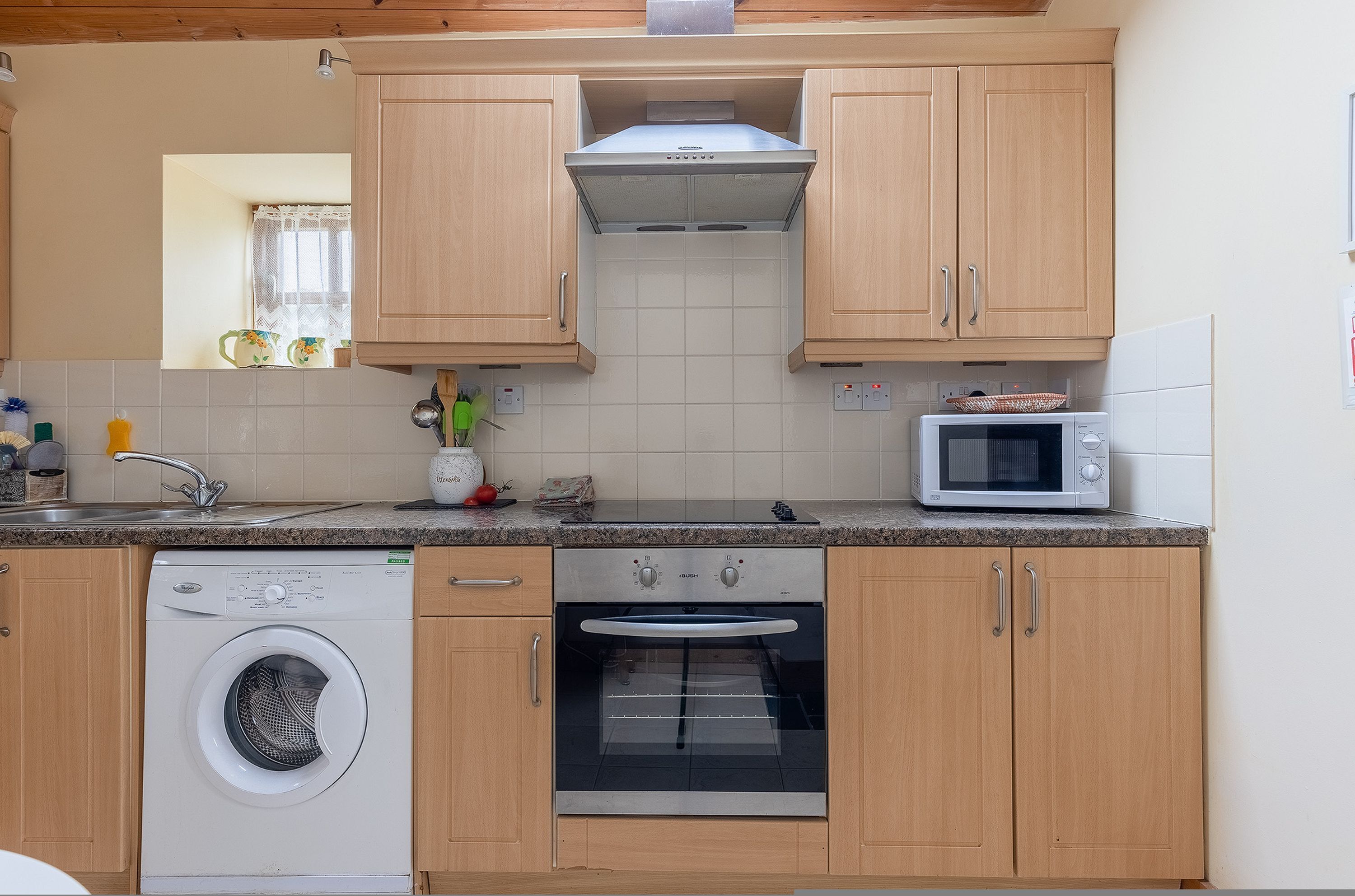 A kitchen with wooden cabinets, a washing machine, an oven, and a microwave.