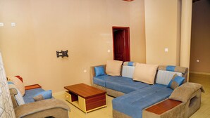 A living room with a sectional sofa, a wooden coffee table, and a small cabinet. - OMX Hotel Remera (Kigali)