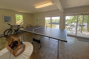 A room with a ping pong table, bicycles, and a view of a balcony with a railing. - Waterfront Home With Dock and Two Water Facing Decks! (2372) (Chatham)