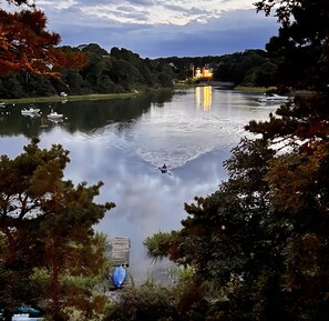 Un lago tranquilo con un muelle y un bote, rodeado de árboles y un edificio iluminado a lo lejos.