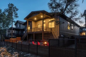 Una casa de madera de varios pisos, con un balcón, una escalera y un área cercada con sillas rojas.