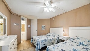 A bedroom with two beds, a dresser, a nightstand, a ceiling fan, and a door leading to a bathroom.