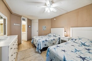 A bedroom with two beds, a dresser, a nightstand, a ceiling fan, and a door leading to a bathroom.
