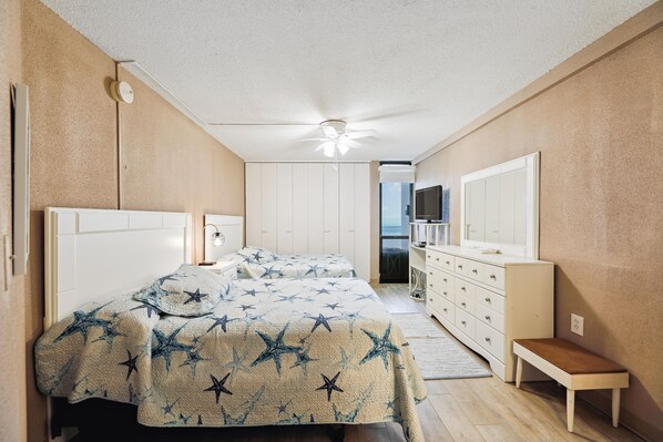 Une chambre à coucher comprenant un lit, des tables de chevet, une commode, un banc et un ventilateur de plafond.