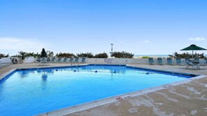 A rectangular swimming pool with a 3 ft deep marking, surrounded by lounge chairs and umbrellas, with a clear sky in the background.