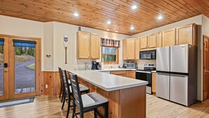 A kitchen with wooden cabinets, a large island with bar stools, a refrigerator, and a microwave. - Lakeside Haus in Presque Isle (Presque Isle)