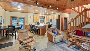 A spacious living area with a wooden ceiling, a kitchen with wooden cabinets, a dining area with a table and chairs, and a staircase leading to an upper level. - Lakeside Haus in Presque Isle (Presque Isle)
