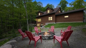 A lodge with a fire pit and red chairs in front.