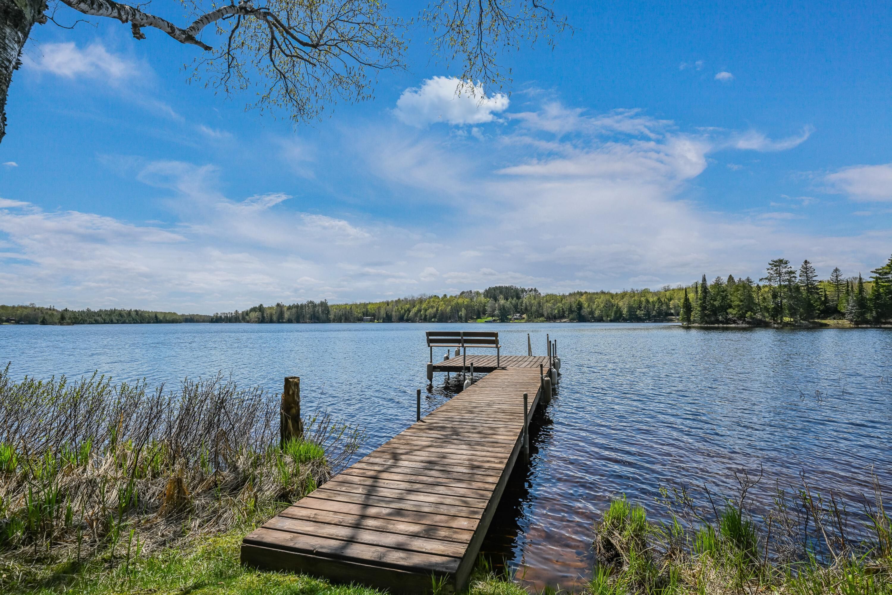 Un muelle de madera se extiende sobre un lago tranquilo con un banco al final.