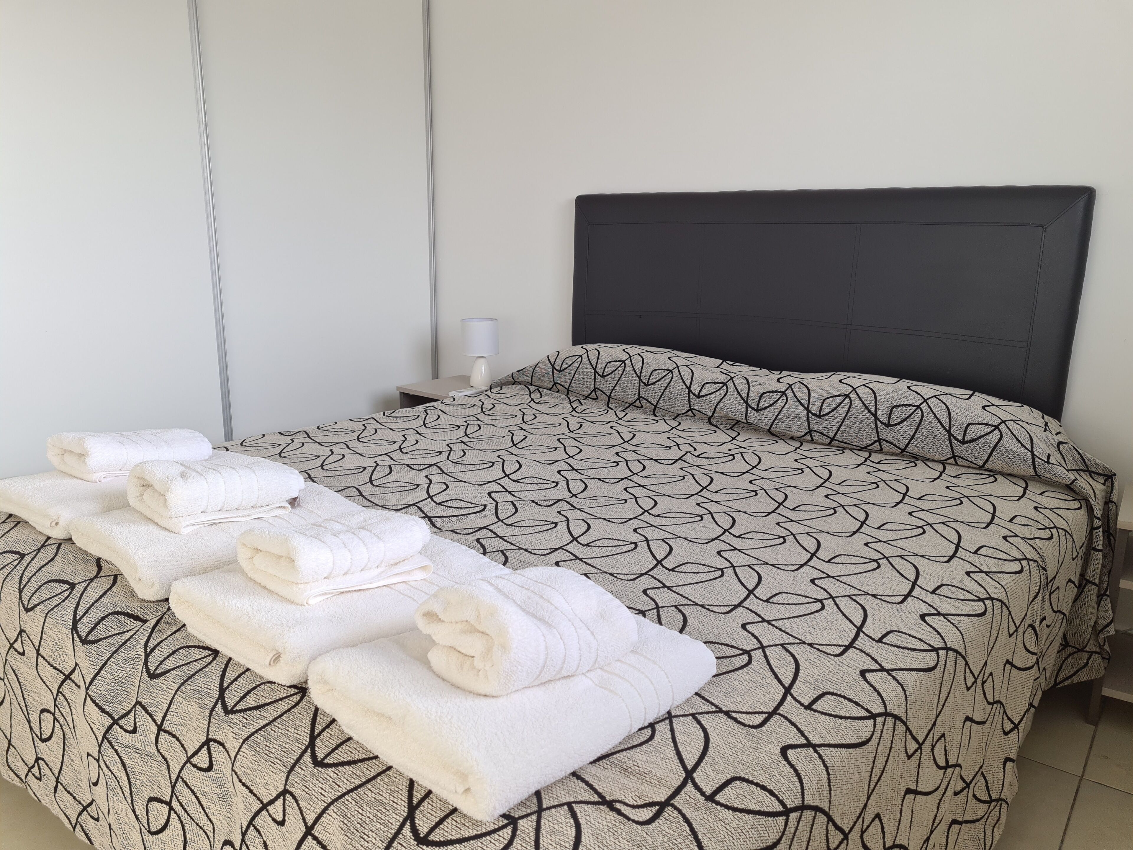 A neatly made bed with a patterned bedspread and rolled towels on the bed.