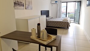 Una habitación de hotel con cama, escritorio, silla, mesa con bandeja y ventana con cortinas.