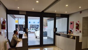 Zona de recepción con separador de vidrio, mostrador de recepción y área de espera con sillas.