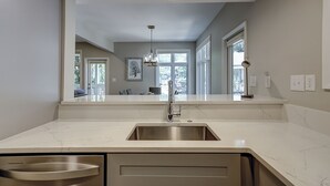 Una cocina con un lavamanos de acero inoxidable, encimera de mármol blanco e iluminación empotrada en el techo.