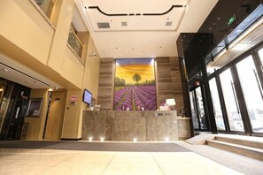 A hotel lobby with a reception desk, a large window, and a mural on the wall.