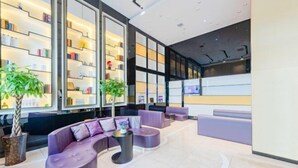 A modern lobby with a curved purple sofa, a small round table, and a bookshelf filled with books and decorative items.