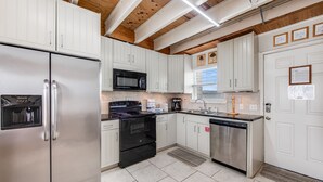 A modern kitchen with white cabinets, stainless steel appliances, and a wooden ceiling.