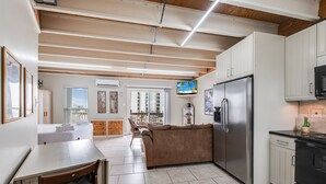 A modern kitchen with white cabinets, a stainless steel refrigerator, and a black stove. There is a dining area with a table and chairs.