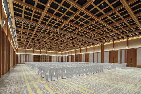 A spacious hall with rows of white chairs, a patterned floor, and a wooden ceiling with a grid design.