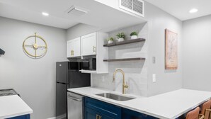 A modern kitchen with white cabinets, a stainless steel refrigerator, a microwave, and a sink with a gold faucet. There are blue cabinets, a wooden countertop, and a bar stool with a gold frame. - Chic Condo Retreat in Central Buckhead Atlanta (Atlanta)