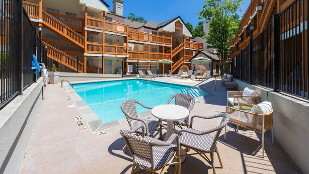 A pool area with lounge chairs and a table, surrounded by wooden buildings with balconies. - Chic Condo Retreat in Central Buckhead Atlanta (Atlanta)