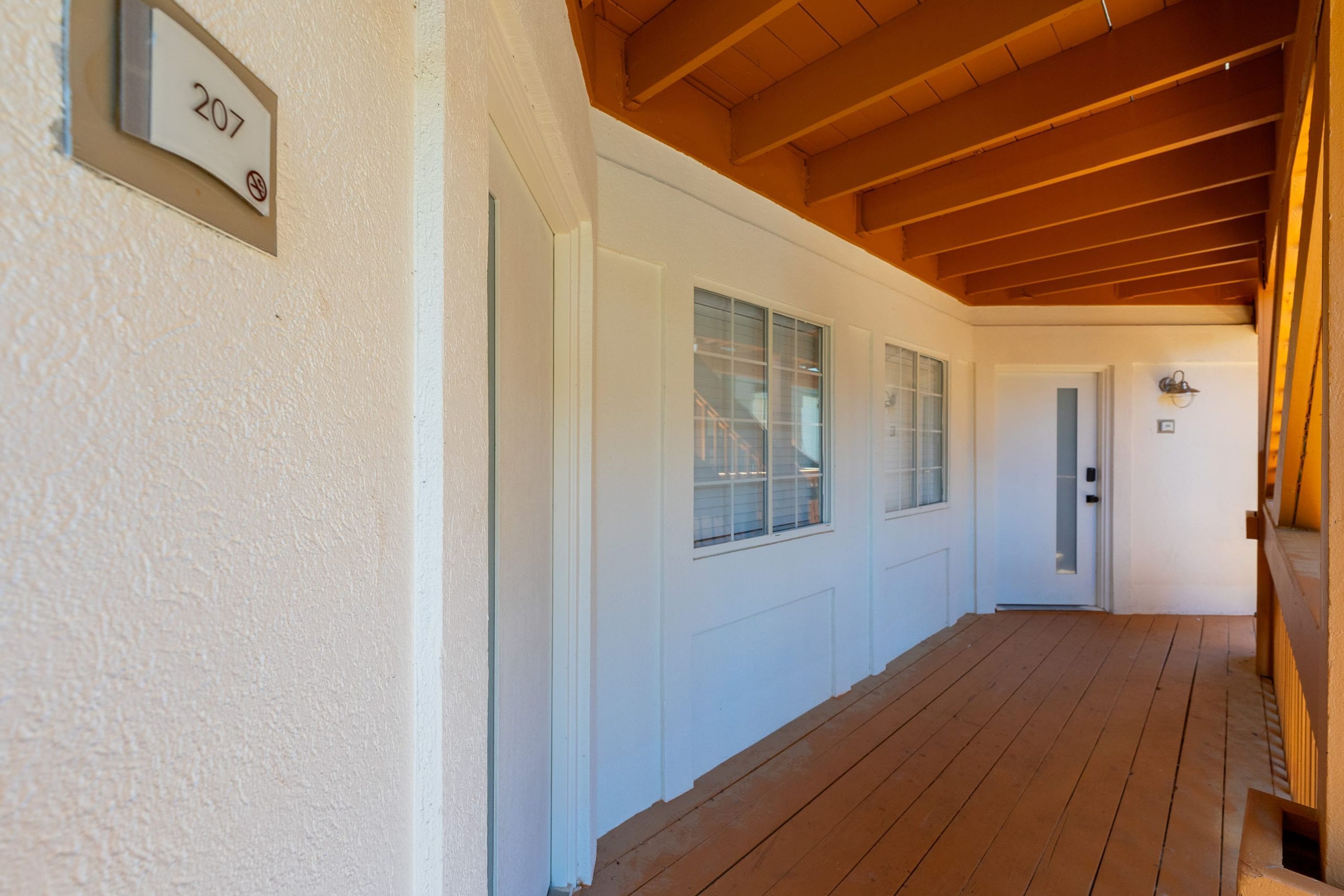 Un pasillo con suelo de madera, paredes blancas y una puerta con el número 207.