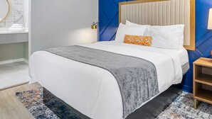 A modern hotel room with a large bed, a blue accent wall, a wooden headboard, and a small bedside table with a lamp. - Chic Condo Retreat in Central Buckhead Atlanta (Atlanta)