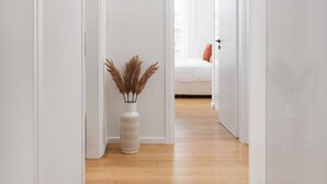 A narrow hallway with wooden flooring leading to a bedroom with a bed and a window. - Athenian Riviera Elegant Residence (Vari-Voula-Vouliagmeni)