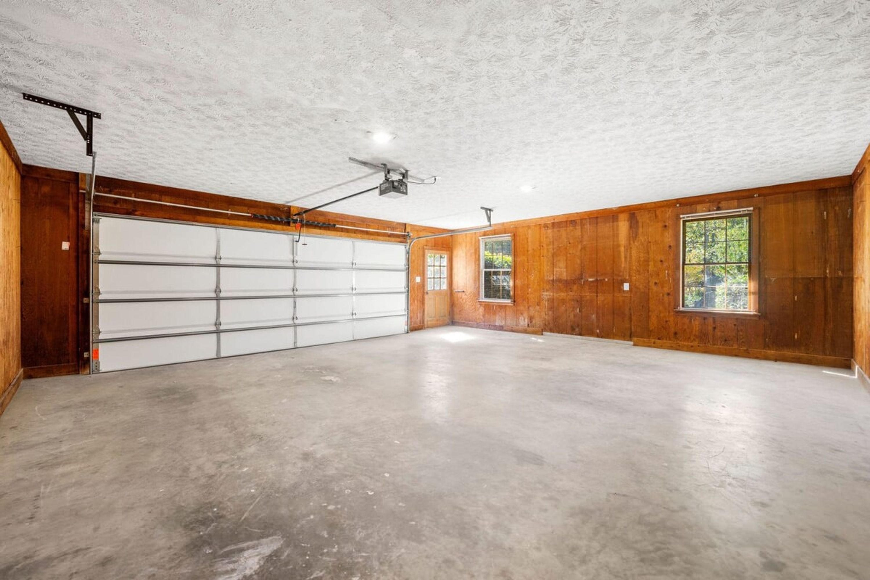 A garage with a ceiling fan, a large white garage door, and wooden walls.
