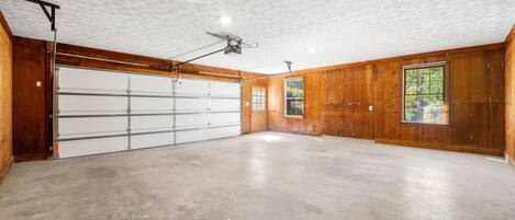 A garage with a ceiling fan, a large white garage door, and wooden walls.