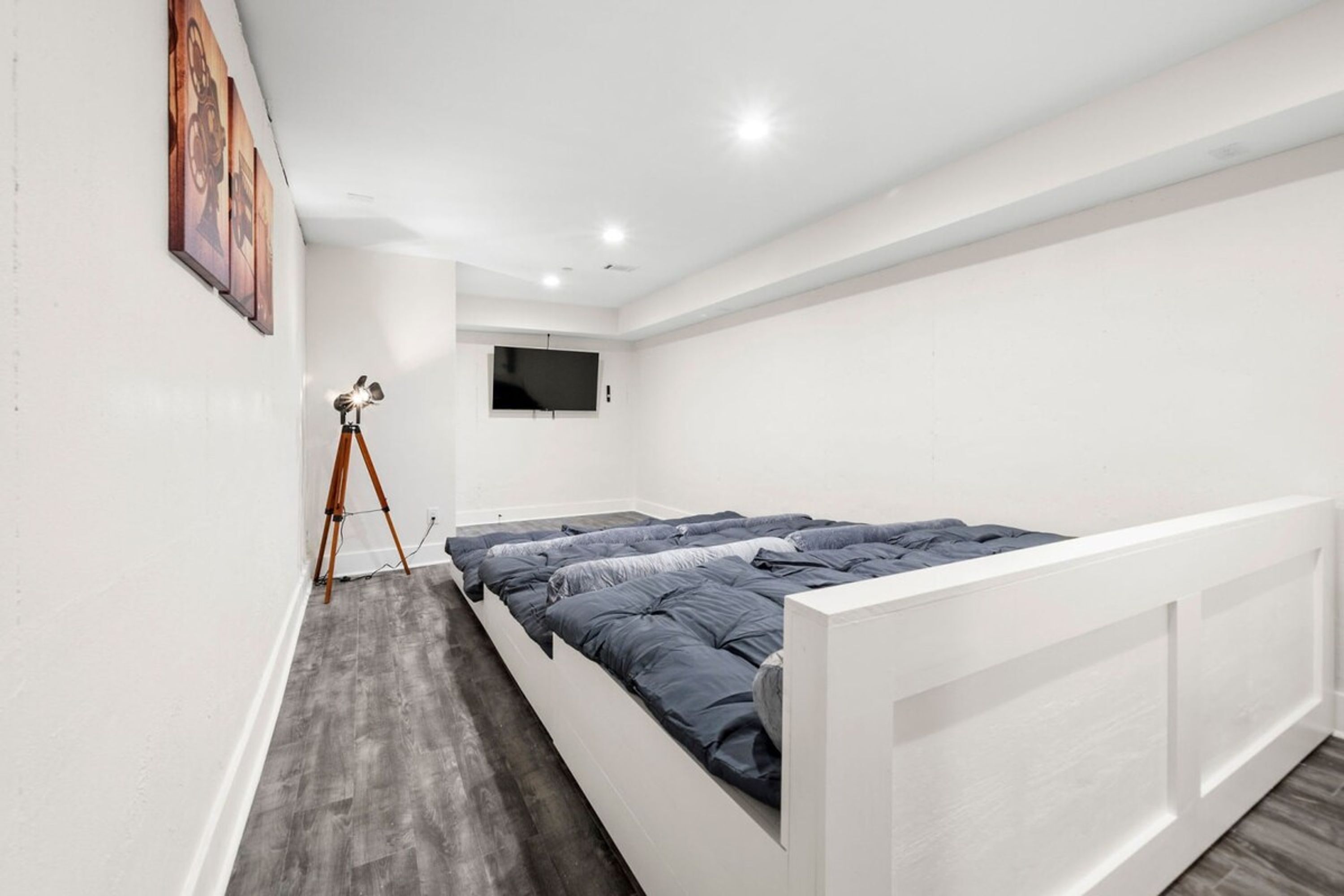 A modern bedroom with a large bed, a mounted TV, and a tripod in the corner.