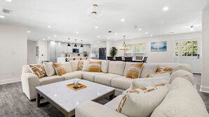 Ein modernes Wohnzimmer mit Ecksofa, Couchtisch und einer Küche im Hintergrund.