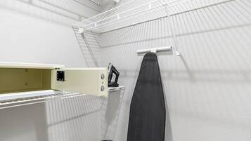 A compact room with a metal bed frame, a shelf unit, and a hanging ironing board.