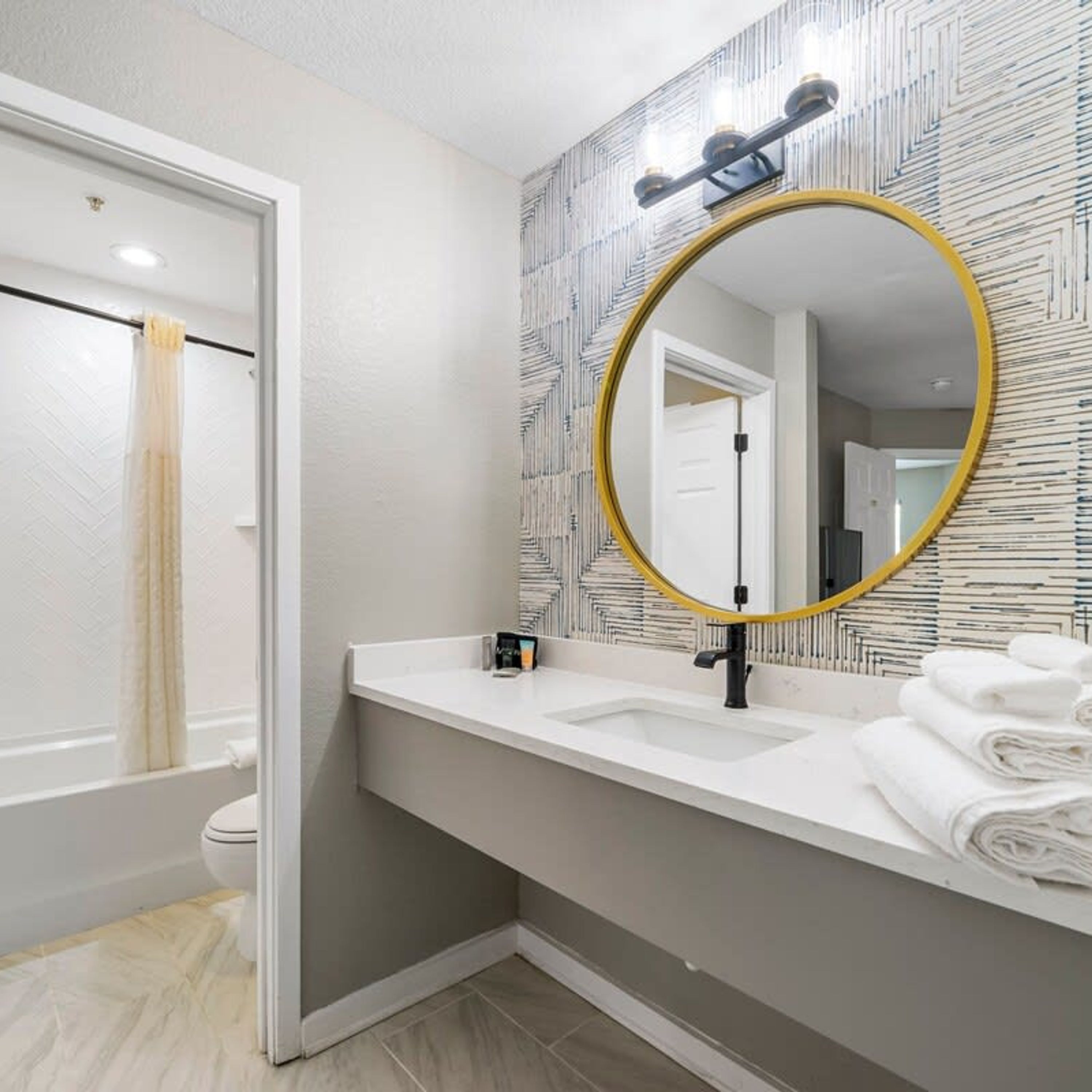 A bathroom with a white sink, a large mirror with a gold frame, and a patterned wall.