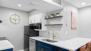 Une cuisine moderne avec des meubles blancs, un réfrigérateur noir, un évier avec un robinet doré et un petit îlot central agrémenté de tabourets de bar.