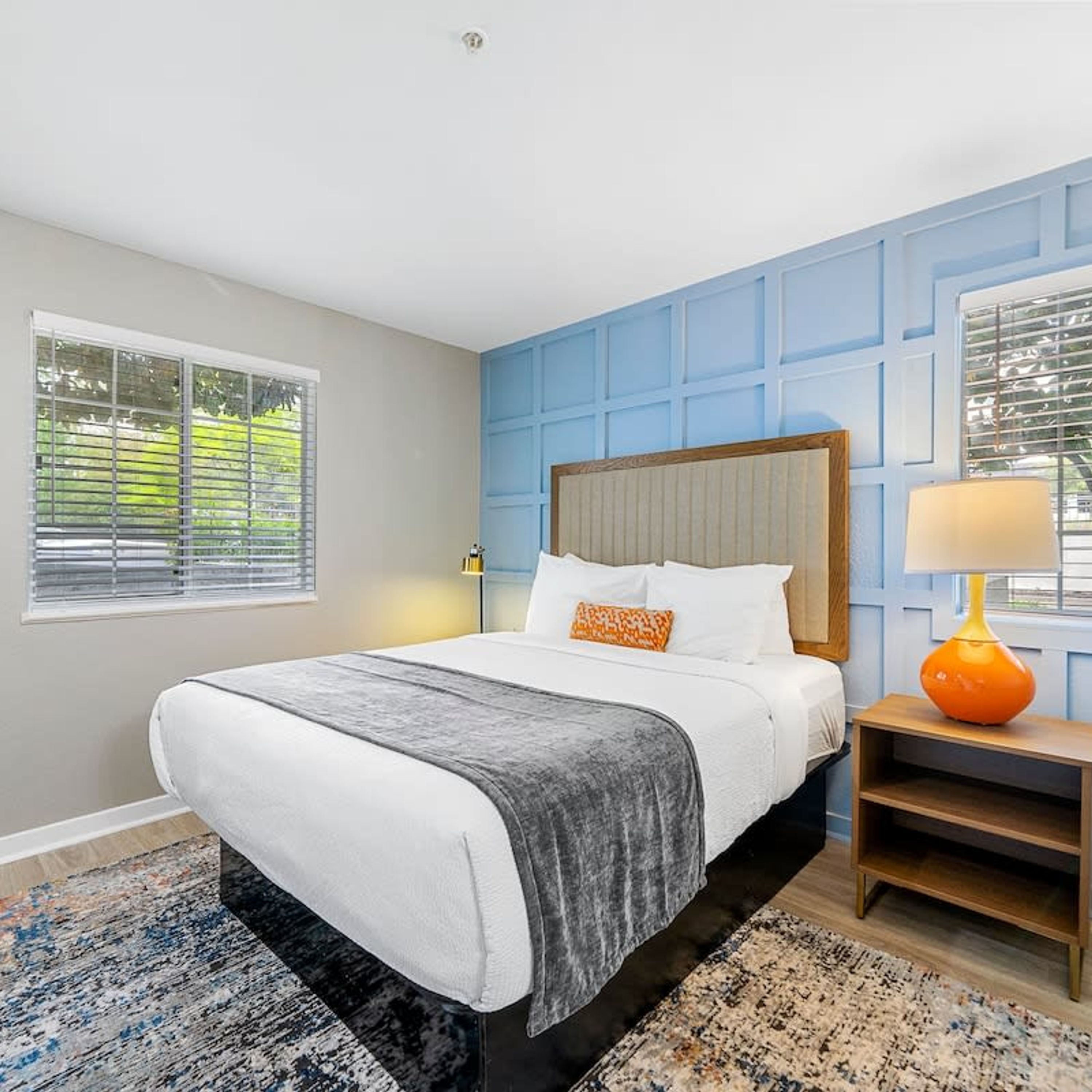 A bedroom with a bed, a nightstand, a lamp, and a window with blinds.