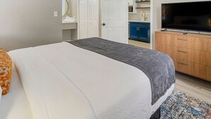 Une chambre à coucher avec un lit, une télévision, une armoire et une salle de bain visible à travers une porte ouverte.