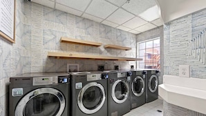 A laundry facility with four washing machines, wooden shelves, and patterned walls. - Newly Renovated Atlanta Gem Central Buckhead Apt (Atlanta)
