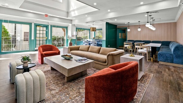A spacious lobby with a high ceiling, a beige sofa, red armchairs, a coffee table, and a dining area with a table and chairs. - Newly Renovated Atlanta Gem Central Buckhead Apt (Atlanta)