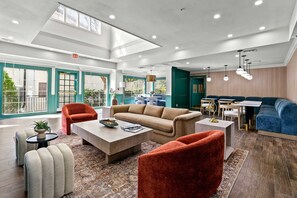 Eine großzügige Lobby mit hoher Decke, einem beige farbenen Sofa, roten Sessel, einem Couchtisch und einem Essbereich mit Tisch und Stühlen.