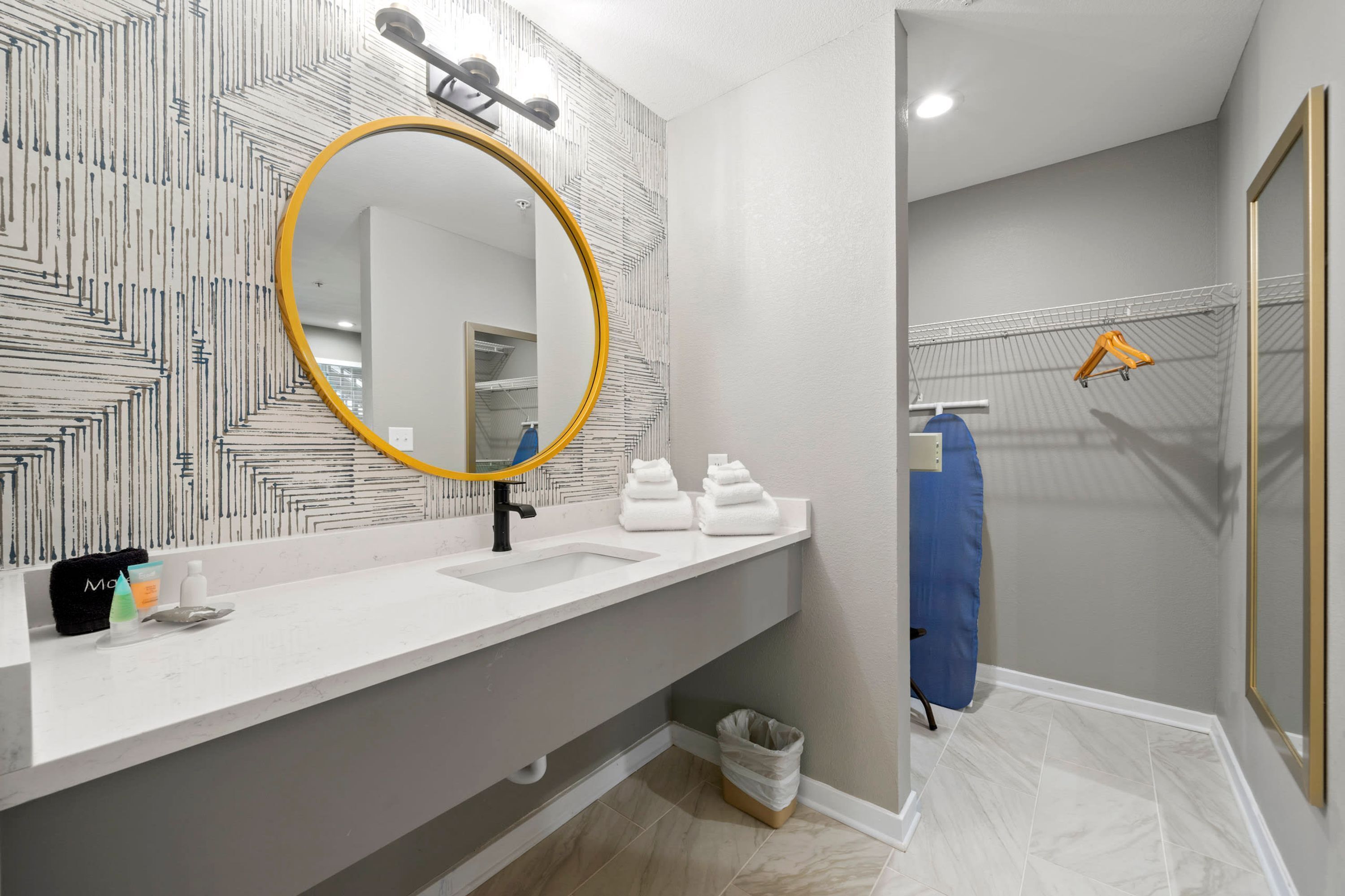 A modern bathroom with a white sink, a round mirror with a yellow frame, and a towel rack with a blue towel.