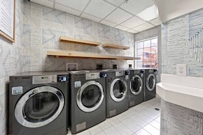 A laundry facility with multiple washing machines, wooden shelves, and patterned walls. - Prime Buckhead Chic Condo in Atlanta (Atlanta)