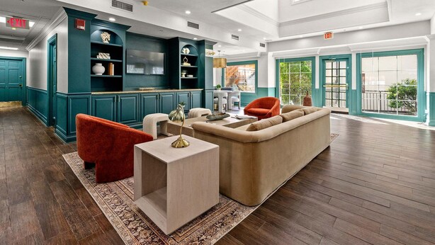 Een ruime lobby met een moderne bank, een rode stoel en een houten salontafel. Er zijn blauwgroene kasten en een groot raam met uitzicht op het landschap.
