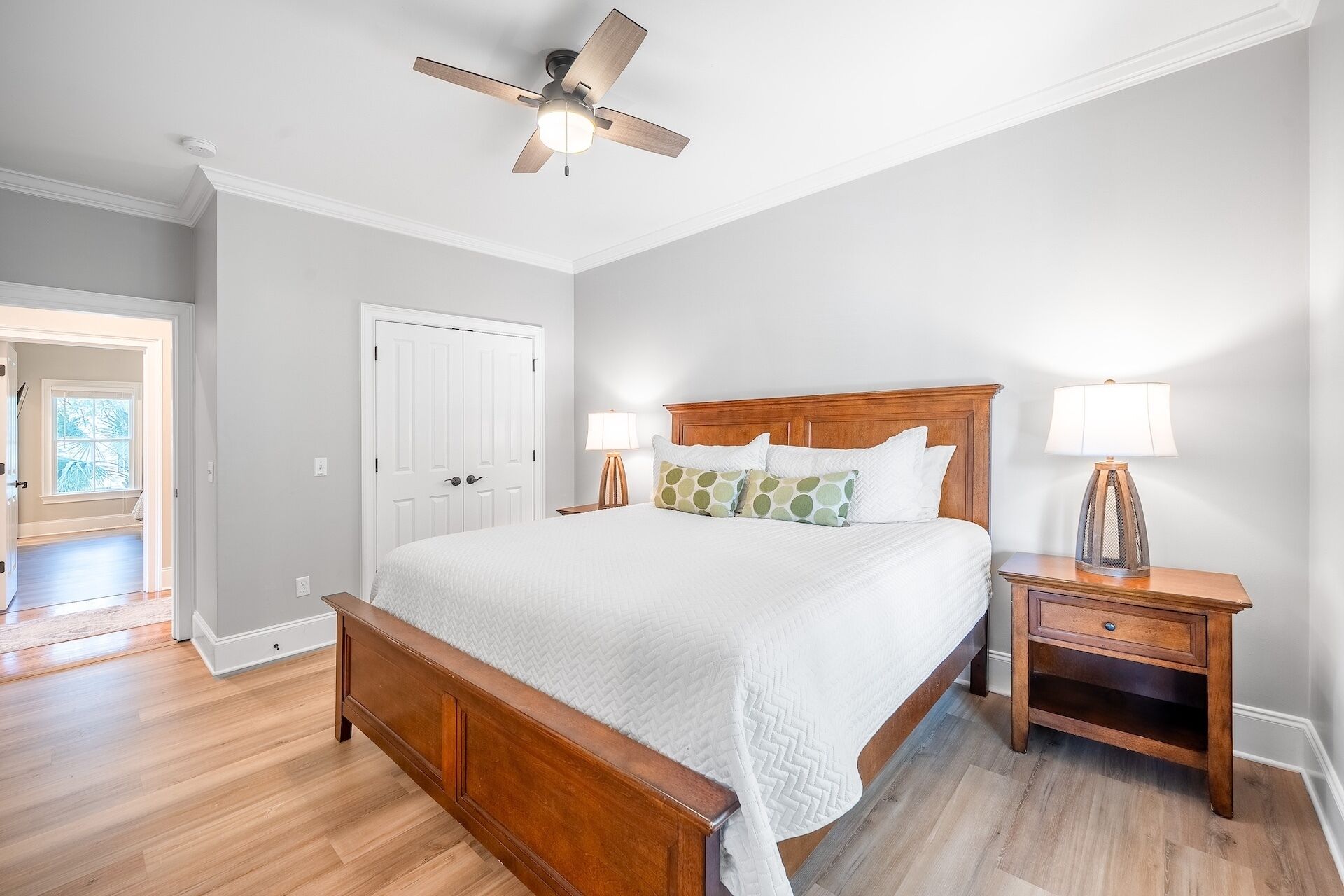 A bedroom with a wooden bed, two bedside tables, a ceiling fan, and a white door.