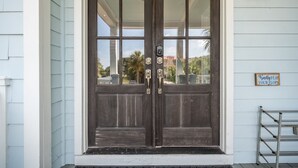 A dark wooden double door with a glass panel, a keypad lock, and a small sign on the wall beside it.